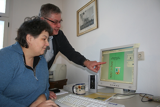 Auf dem Computerbildschirm von Bürgerarbeiterin Manuela Beesdo ist das Deckblatt der neuen Ortschronik zu sehen. Im Hintergrund: Ortsvorsteher Otto-Heinz Lehmann