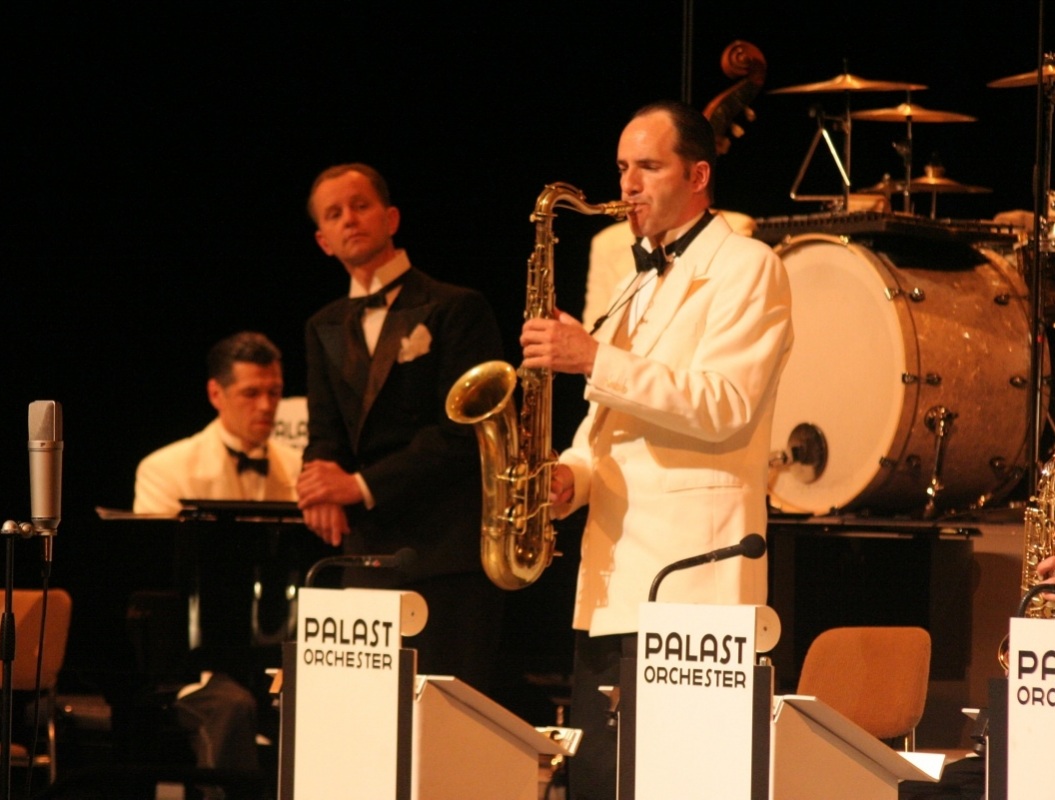 Max Raabe (im schwarzen Frack) betrachtet mit höflichem Interesse das solistische Tun des Saxophonisten seines Palast-Orchesters. Am 3. Februar ist er wieder in der Lausitzhalle zu Gast. Foto: Julia Lindenberger (A)