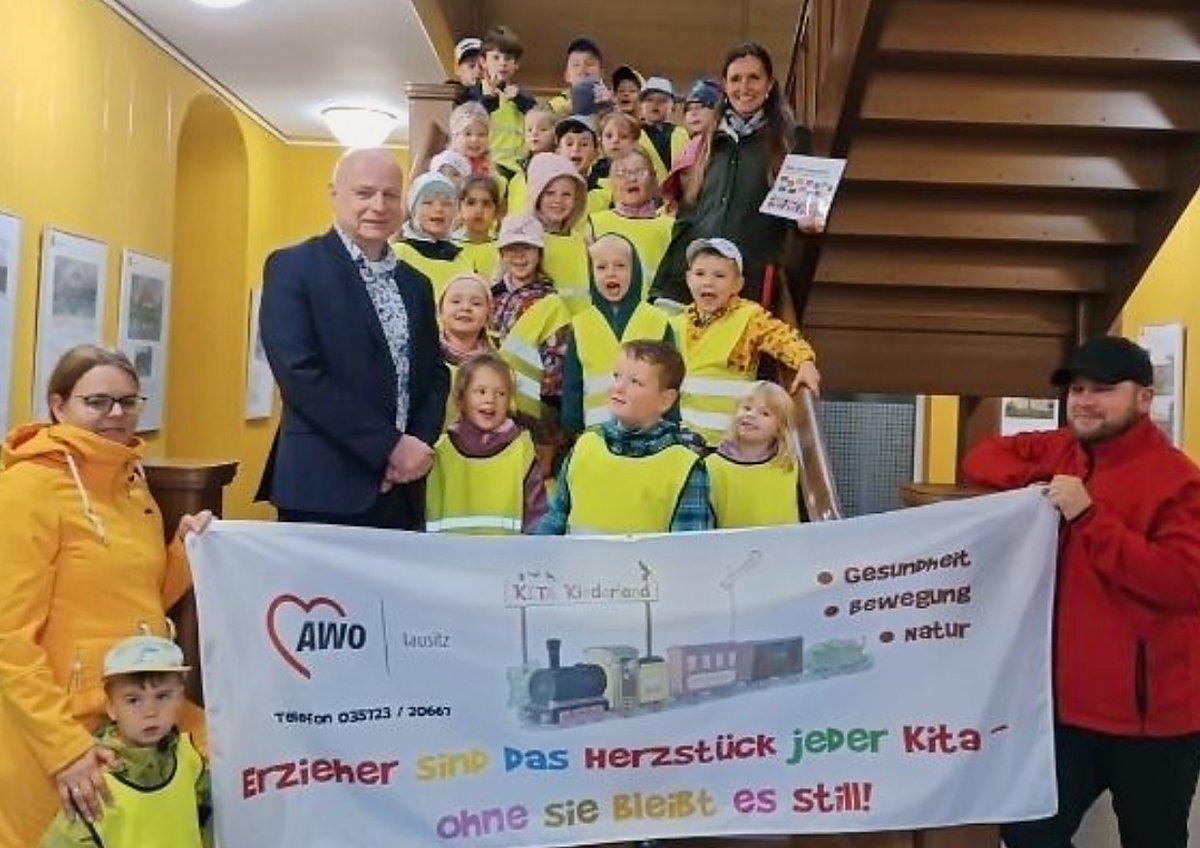 Man sieht Bürgermeister Harry Habel, die Kita-Kinder und ein Transparent mit der Aufschrift Erzieher sind das Herzstück jeder Kita.