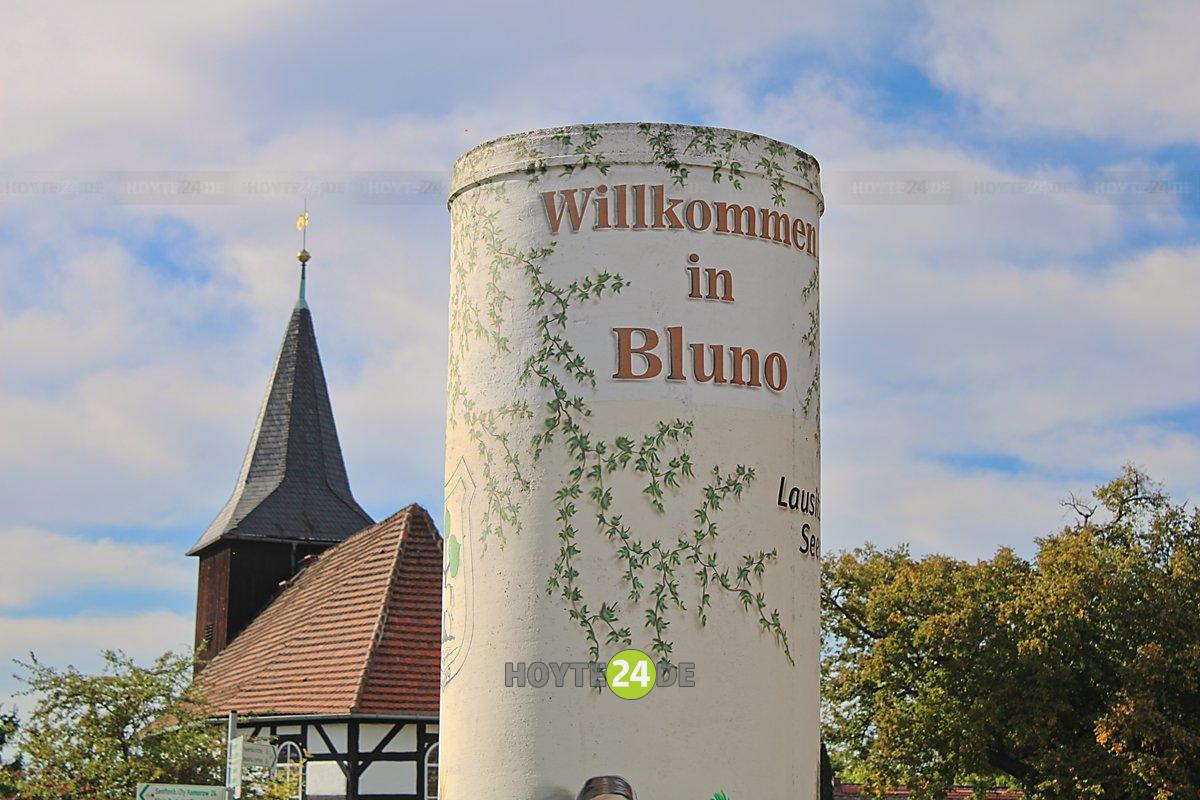 Man sieht die Kirche und ein Willkomensschild in Bluno.