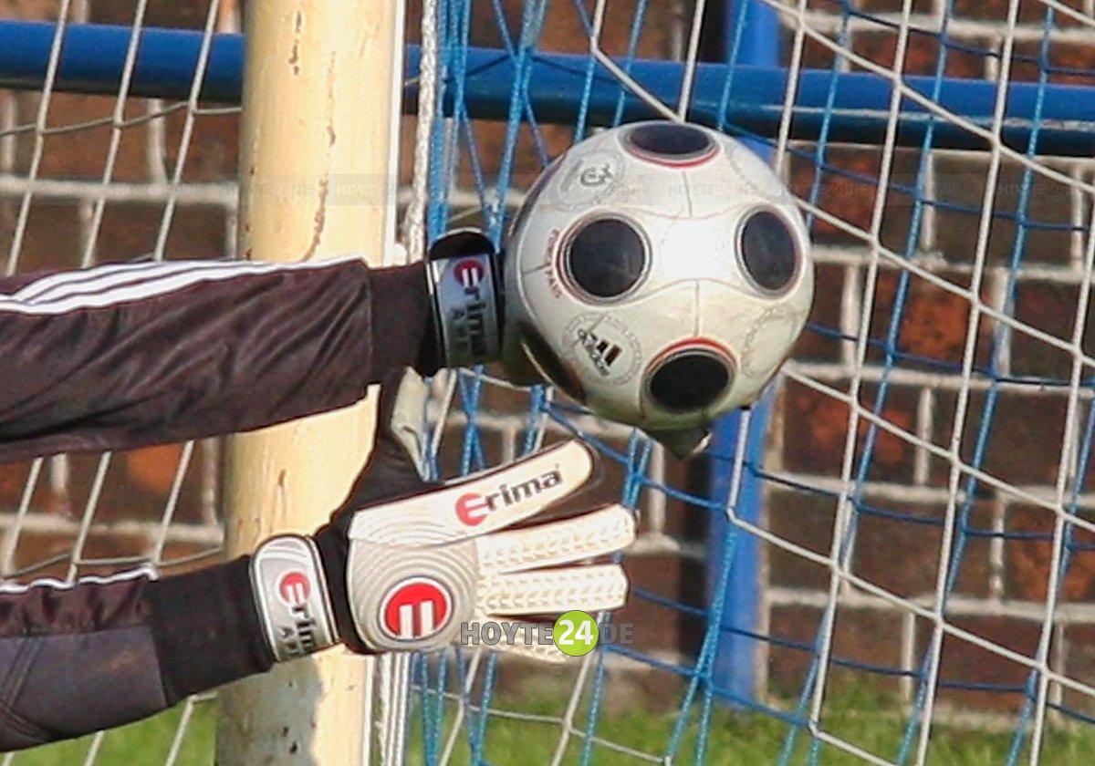 Man sieht einen Fußball mit den Armen eines Tormannes.