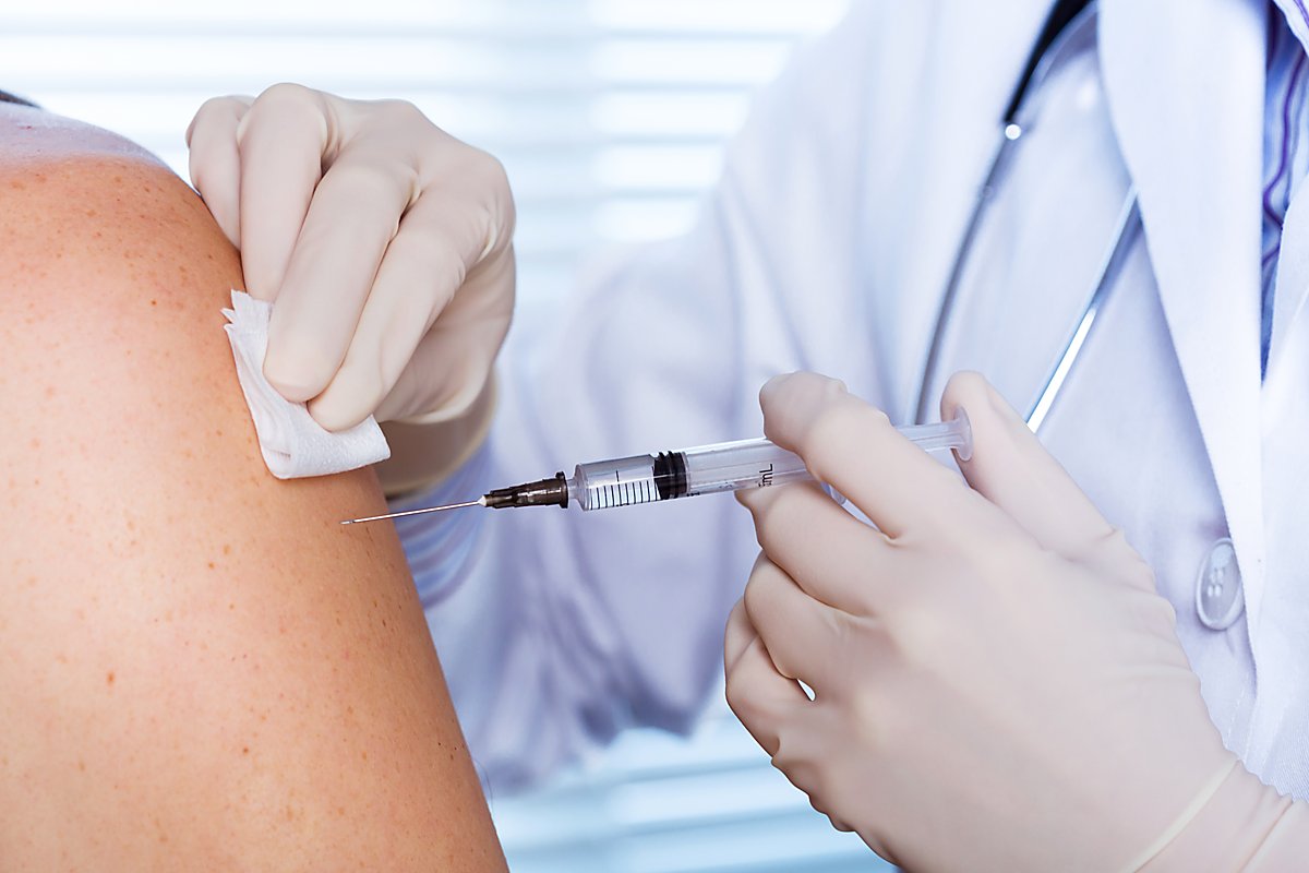 Man sieht einen Arzt beim Impfen und einen Patienten-Arm.