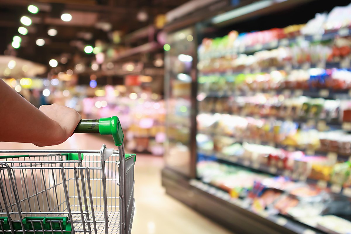 Man sieht, wie jemand einen Einkaufskorb durch einen Supermarkt schiebt.