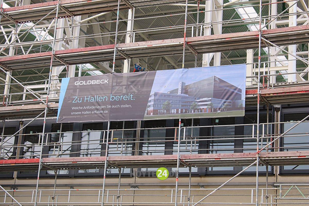 Man sieht ein Detail und ein Schild mit der Ansicht des fertigen Campus.
