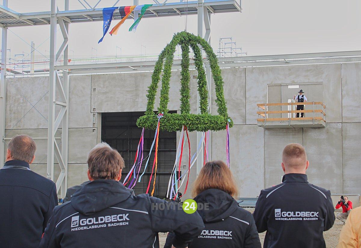 Man sieht den Richtkranz, Menschen mit Goldbeck-Jacken sowie ZimmermannTilo Schelenz beim Richtspruch.