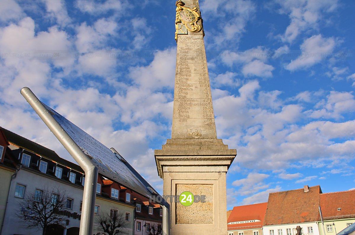Man sieht die Postmeilensäule in Wittichenau mit dem Krabat-Weg-Schild