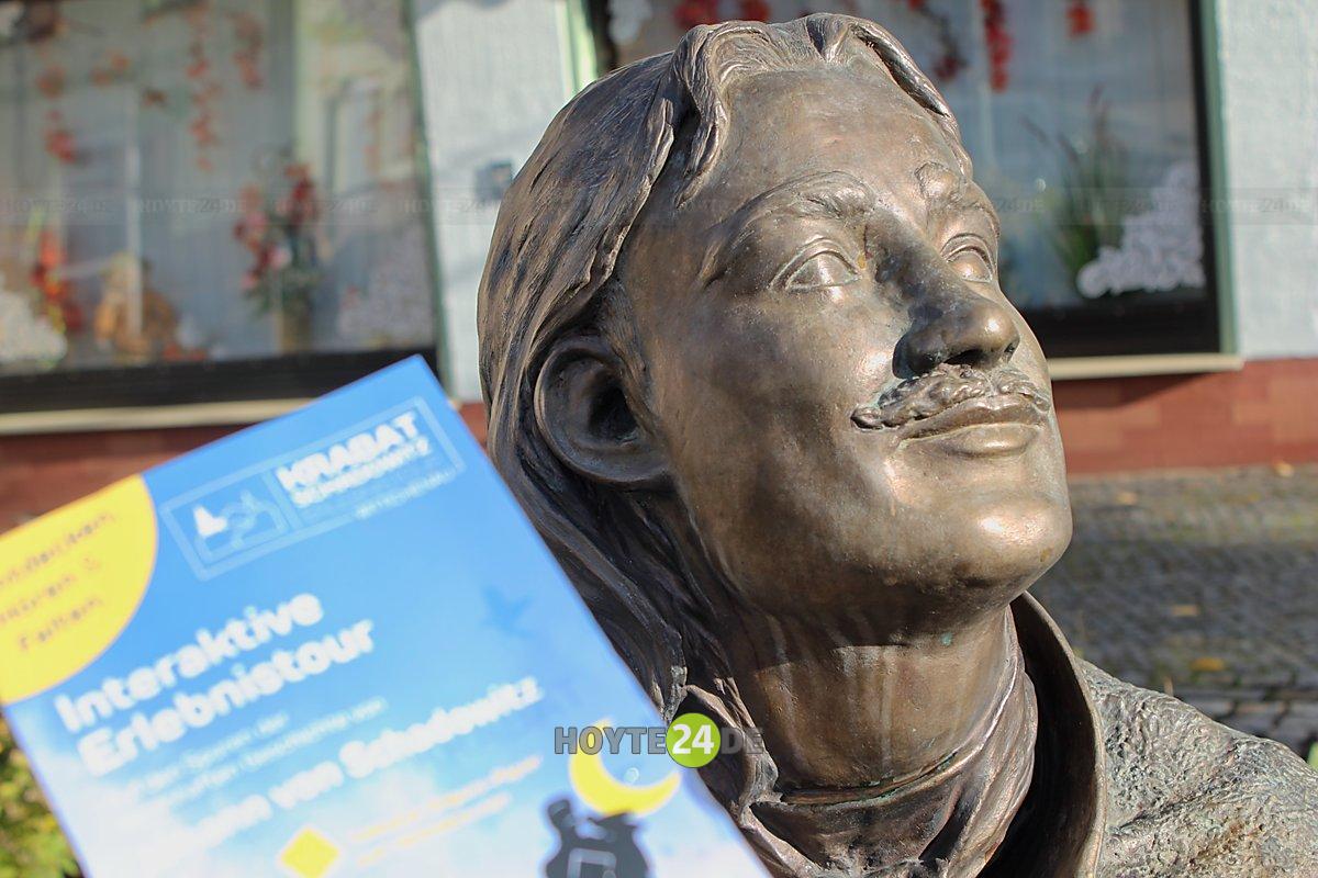 Man sieht die Krabat-Plastik in Wittichenau mit dem Flyer zum Krabat-Erlebnisweg.