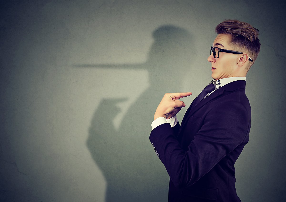 Man sieht einen Mann, dessen Schatten eine Lügen-Nase hat.