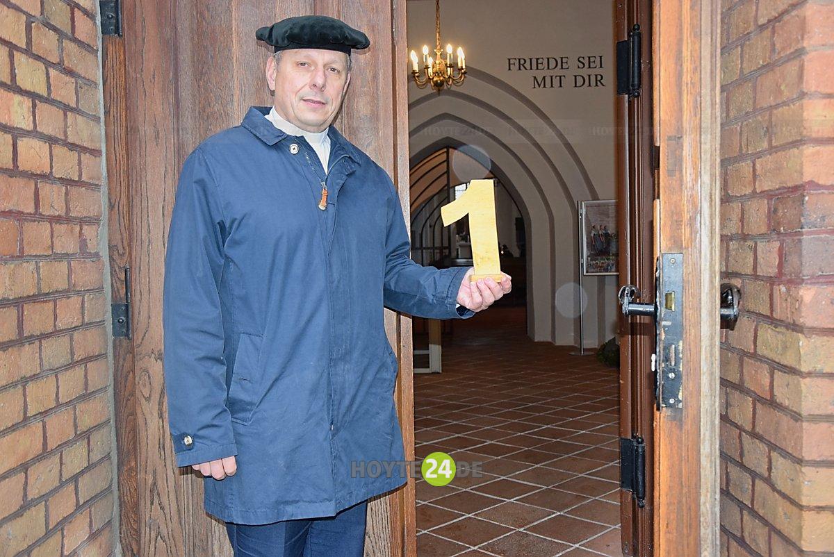 Man sieht Torsten Vogel mit einer 1 in der Hand vor der Johanneskirche stehen.
