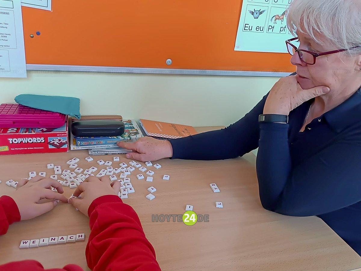 Man sieht eine Lesementorin und Kinderhände, die einen Haufen Buchstaben sortieren.