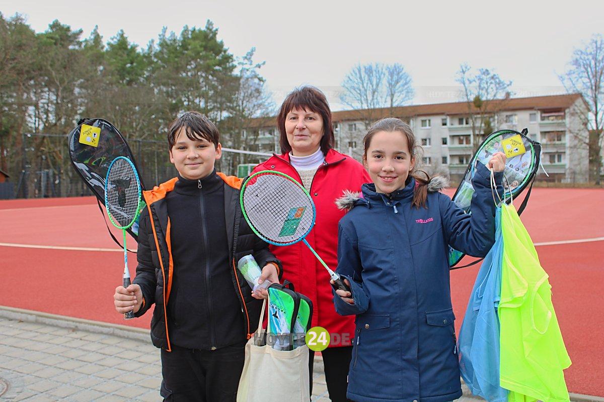 Man sieht Schulleiterin Ines Förster sowie Roman und Paula mit Federballspielen und Leibchen auf dem neuen Sportplatz.