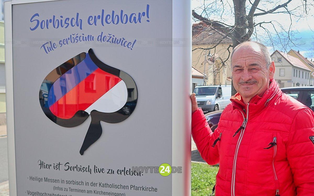 Man sieht Stephen Rachel am Schild "Sorbisch erlebbar!" in Wittichenau.