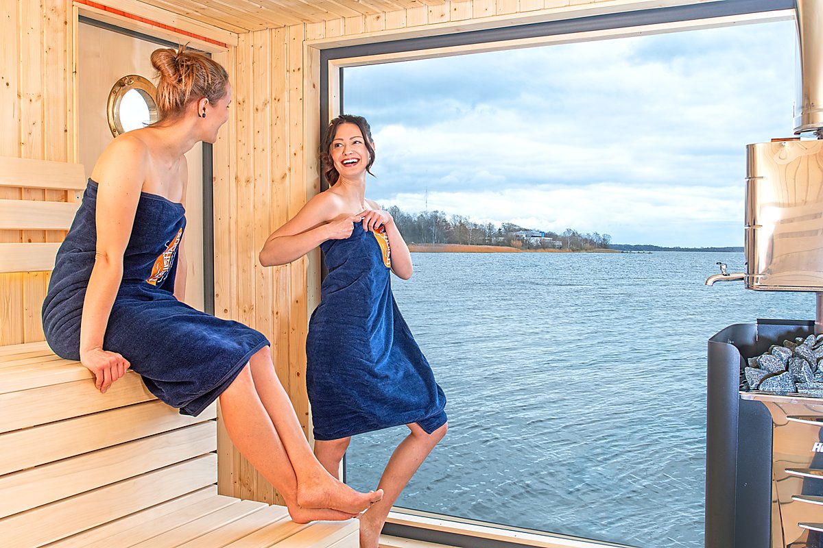Man sieht zwei Frauen in einer Sauna vor einem Panoramafenster mit Blick auf den Senftenberger See.