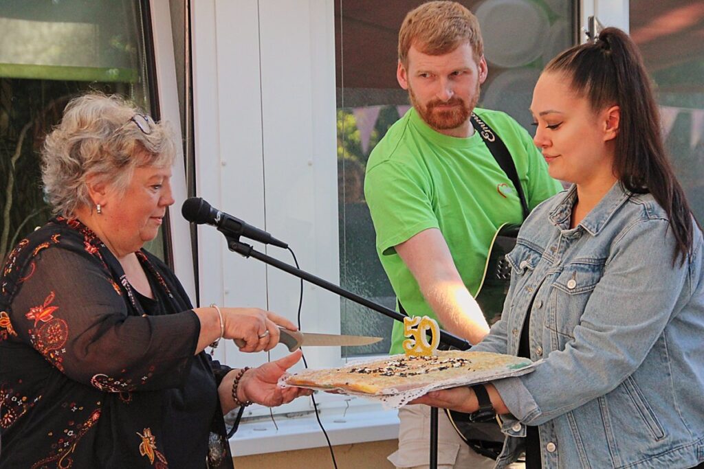 Auf dem Bild wird eine Geburtstagstorte mit einer großen 50 angeschnitten.