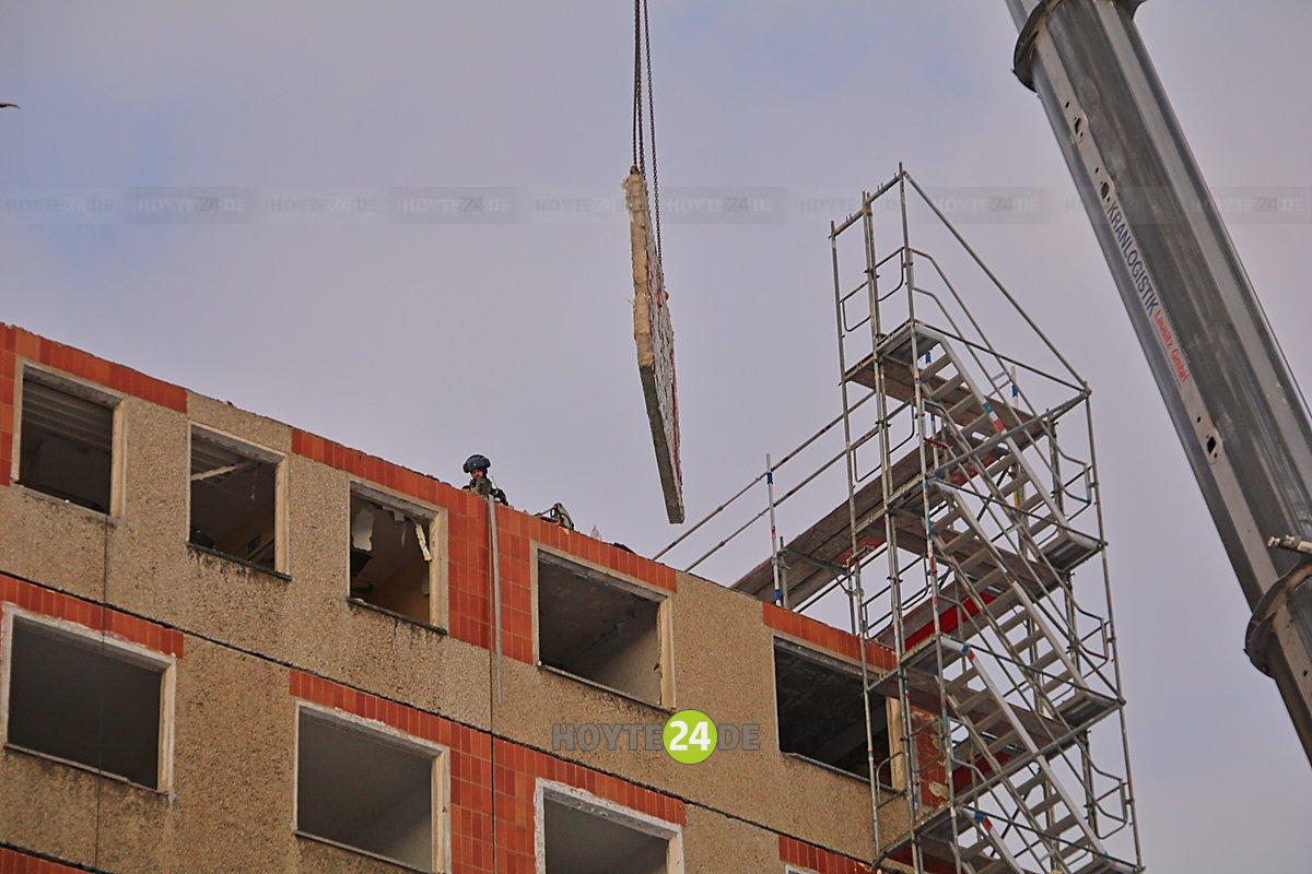 Man sieht, wie der Kran eine Platte vom Hochhaus am Knie hebt.
