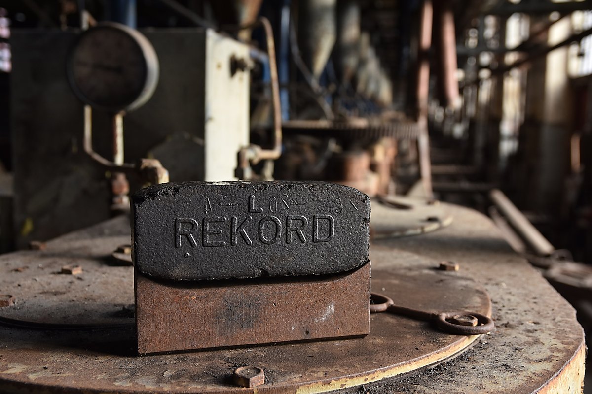 Man sieht ein Rekord-Brikett vor dem Hintergrund der Anlagen der ehemaligen Brikettfabrik Knappenrode.