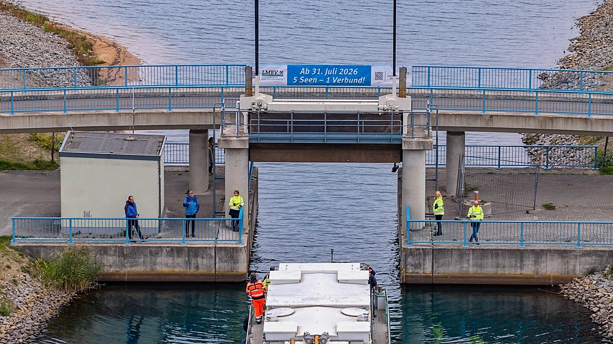 Man sieht ein Banner am Rosendorfer Kanal zwischen Partwitzer See und Sedlitzer See mit einem Banner "Ab 31. Juli 2026 - 5 Seen - 1 Verbund!"
