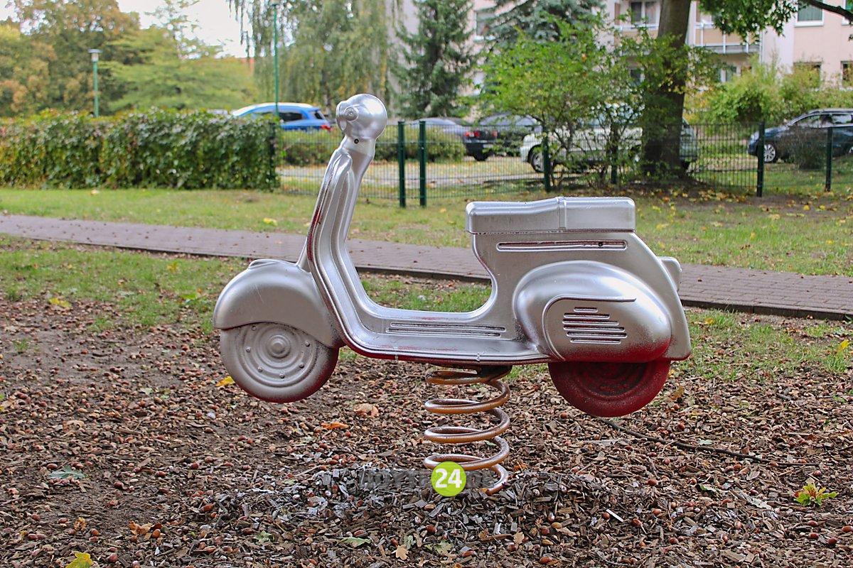 Man sieht ein mit silberner Farbe angesprühtes Spielzeugmotorrad auf einer Wippfeder.