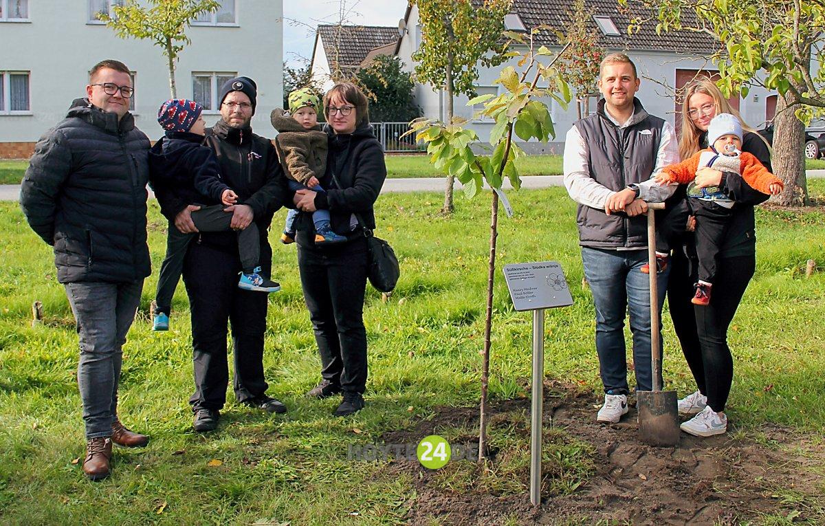 Man sieht drei Kinder mit ihren Familien am neuen Baum.